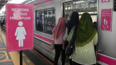 Penumpang perempuan naik ke gerbong khusus wanita KRL di stasiun dengan papan penanda berwarna pink.
