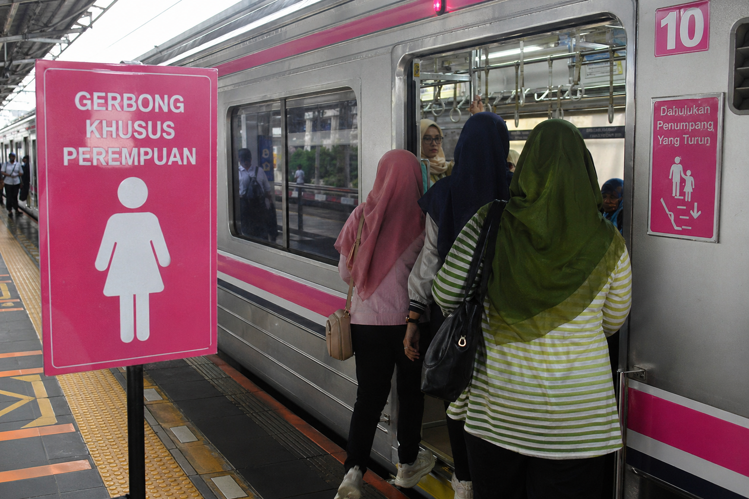 Penumpang perempuan naik ke gerbong khusus wanita KRL di stasiun dengan papan penanda berwarna pink.